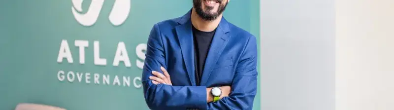 Eduardo Carone, CEO e cofundador da Atlas Governance, sorrindo de braços cruzados em frente ao logotipo da Atlas Governance