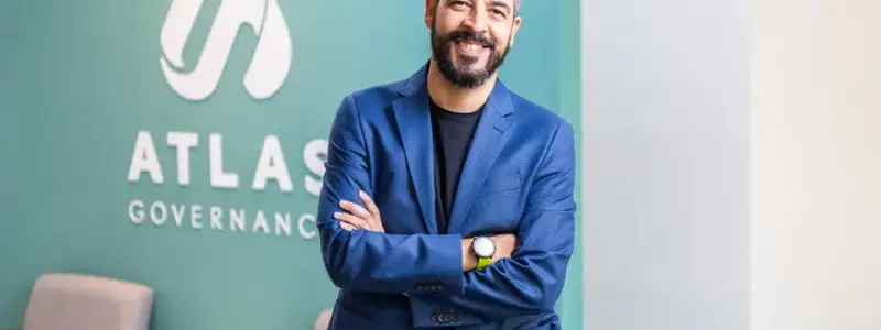 Eduardo Carone, CEO e cofundador da Atlas Governance, sorrindo de braços cruzados em frente ao logotipo da Atlas Governance