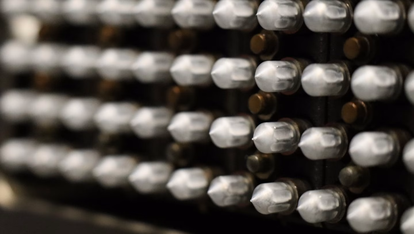 Close-up of a series of white cylindrical pegs on a dark surface, arranged in a grid pattern, with some out-of-focus pegs in the background.