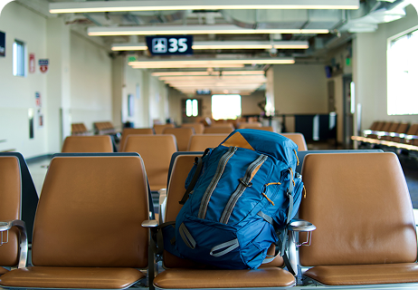 Ein blauer Rucksack steht auf einer leeren Reihe brauner Sitze in einem Wartebereich des Flughafens, unter einem Gate-Schild mit der Nummer 35.