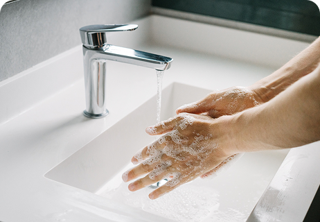 Hände, die unter fließendem Wasser aus einem modernen Wasserhahn am Waschbecken mit Seife eingerieben werden, was auf das Händewaschen hindeutet.