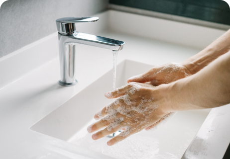 Eine Person, die sich in einem weißen Waschbecken unter fließendem Wasser die Hände mit Seife wäscht.