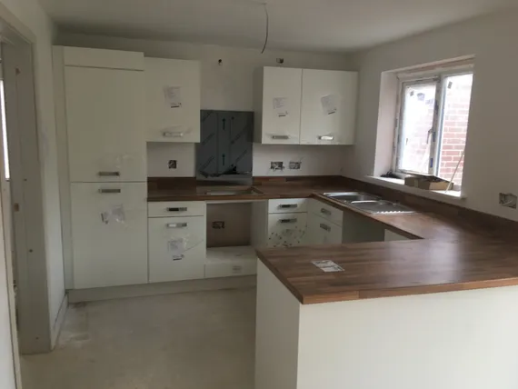 A modern kitchen under construction with white cabinets, wood countertops, and a large window providing natural light.
