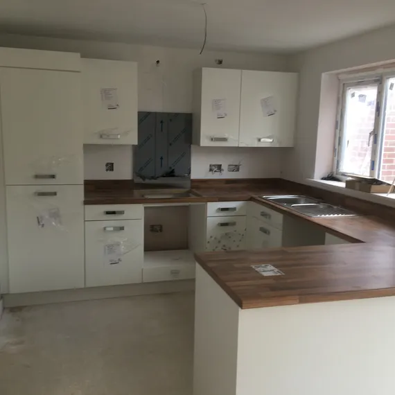 A modern kitchen under construction with white cabinets, wood countertops, and a large window providing natural light.