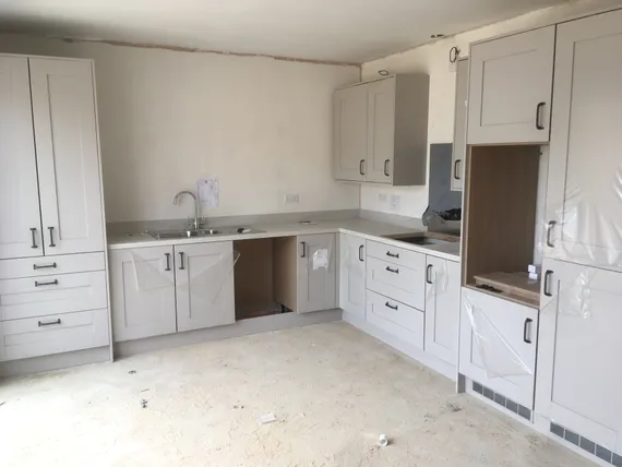 A newly installed kitchen with white cabinets, a sink, and a partially constructed counter in an unfinished room.