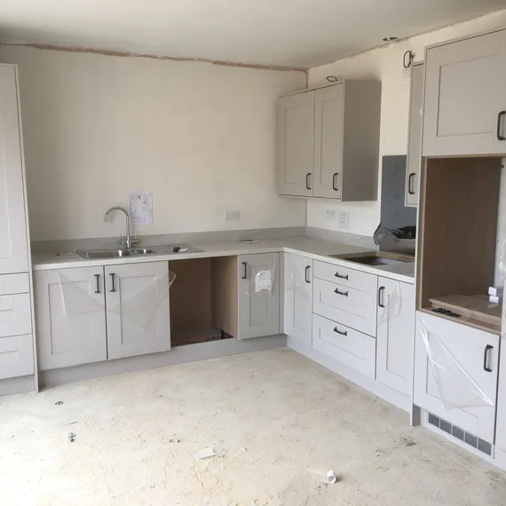 A newly installed kitchen with white cabinets, a sink, and a partially constructed counter in an unfinished room.