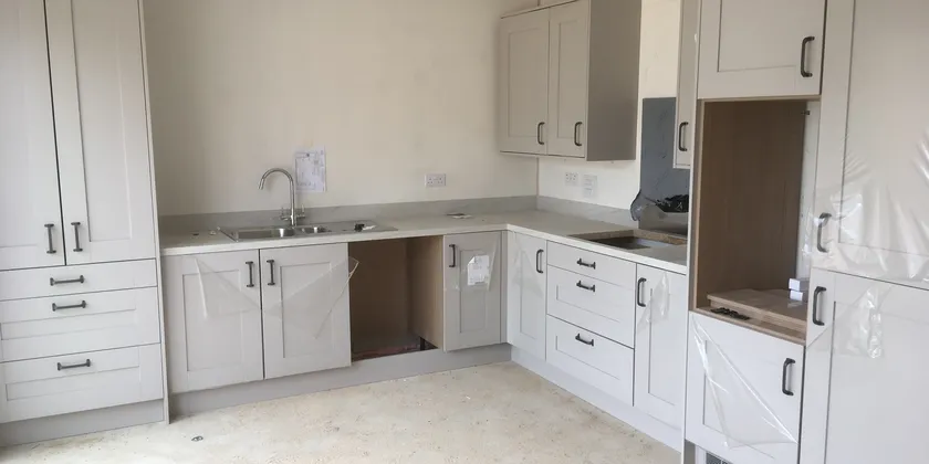 A newly installed kitchen with white cabinets, a sink, and a partially constructed counter in an unfinished room.