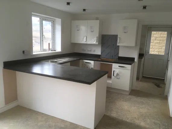 Modern kitchen with white cabinets, dark countertops, and a center island. Unfinished floors and a window provide natural light.