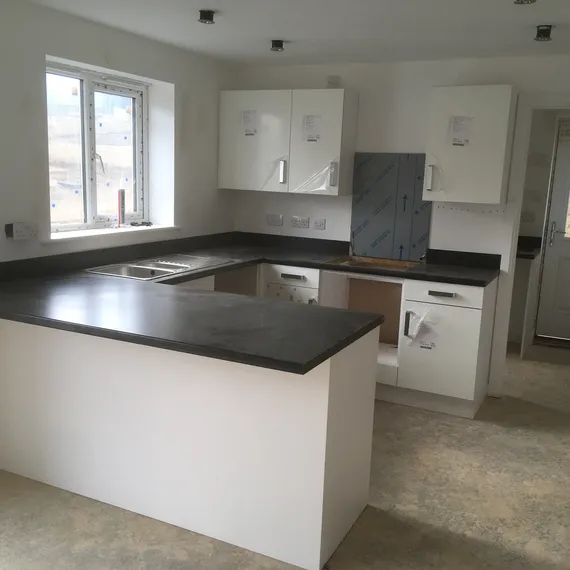 Modern kitchen with white cabinets, dark countertops, and a center island. Unfinished floors and a window provide natural light.