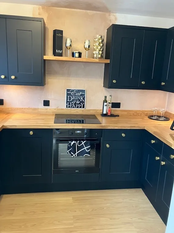 Modern kitchen with dark cabinets, wooden countertops, electric stove, and decor including wine bottles, glasses, and a chalkboard sign.