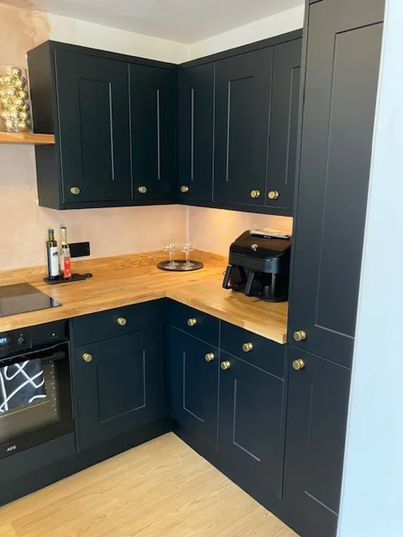 Modern kitchen with dark cabinets, wooden countertops, an air fryer, spice bottles, and oven. Bright and sleek design with gold knobs.