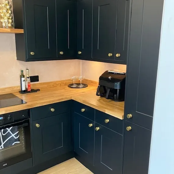 Modern kitchen with dark cabinets, wooden countertops, an air fryer, spice bottles, and oven. Bright and sleek design with gold knobs.