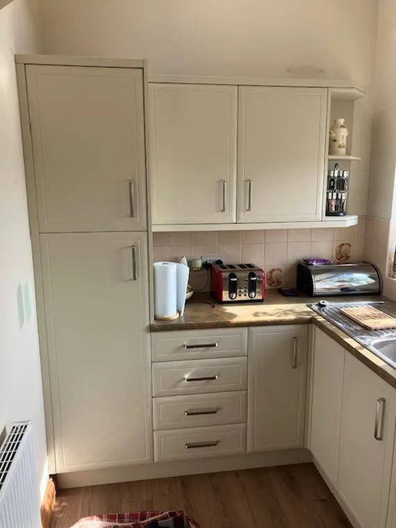 Modern kitchen with cream cabinets, red toaster, paper towels, and a bread bin on a wooden countertop. Sunlight illuminating the room.