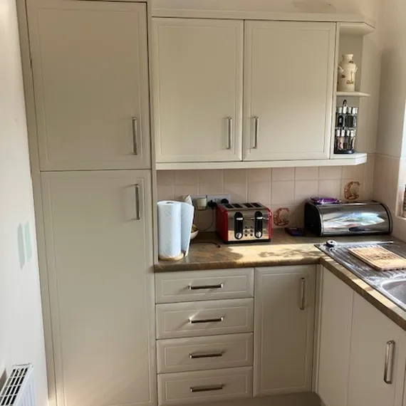 Modern kitchen with cream cabinets, red toaster, paper towels, and a bread bin on a wooden countertop. Sunlight illuminating the room.
