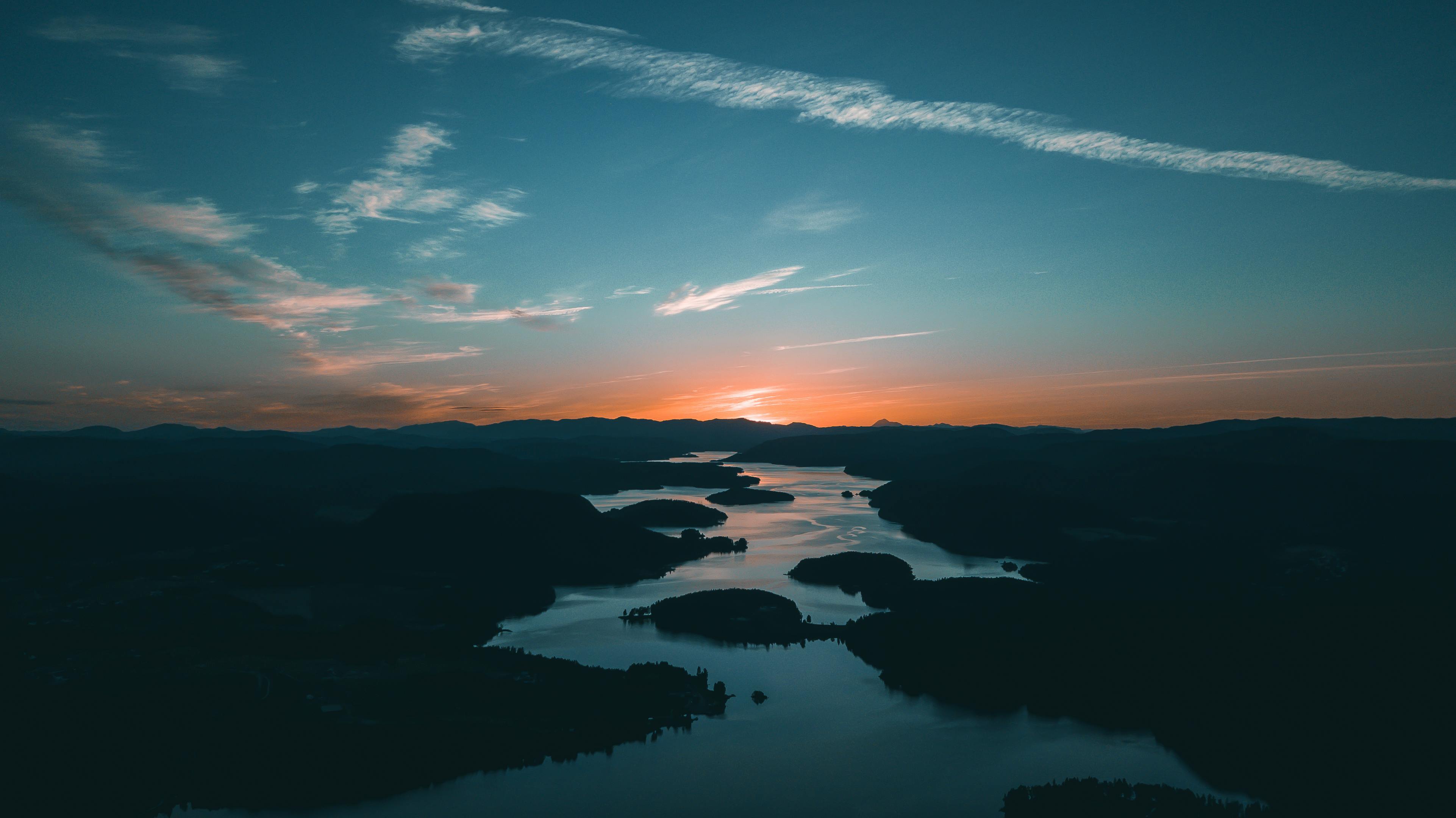Luftaufnahme einer Flusslandschaft mit mehreren Inseln und dunklen Bergen im Hintergrund bei Sonnenuntergang, orangefarbener Himmel und ruhiges Wasser.