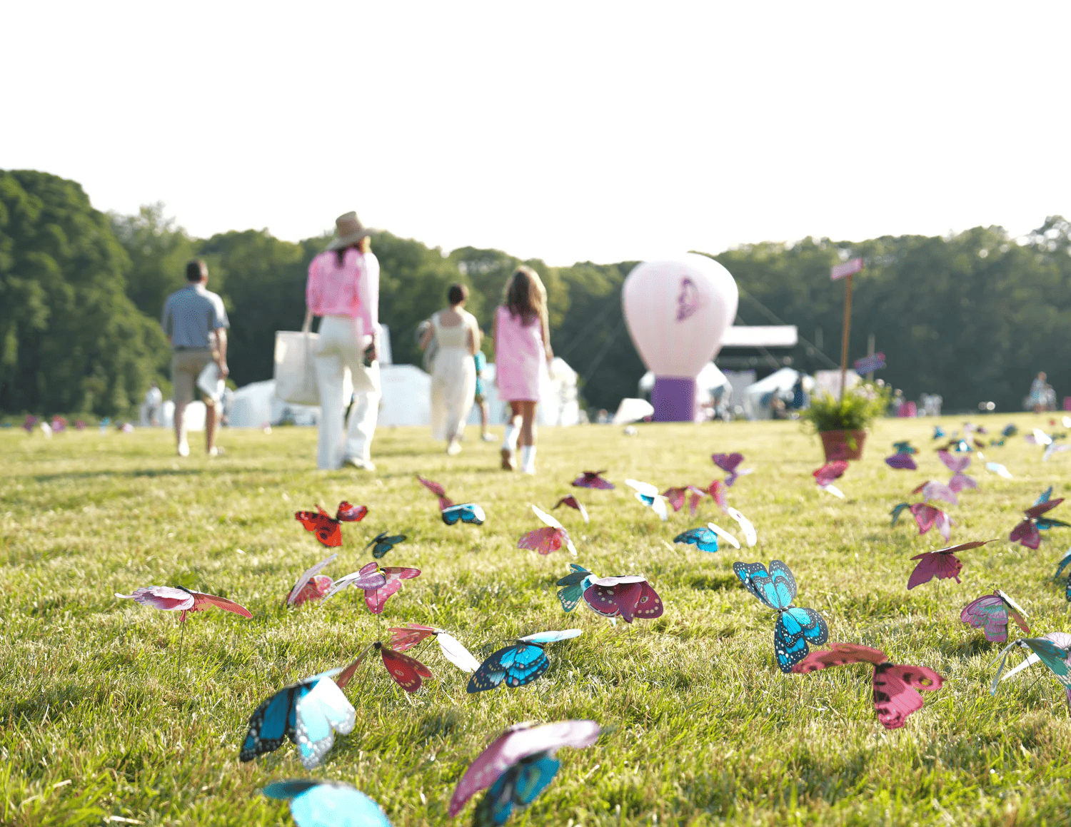 Colorful butterfly decorations scattered across a sunny green lawn at an outdoor festival with people walking in the background.