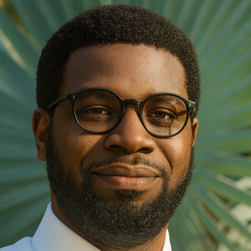 A man with short hair, beard, and round black glasses smiling slightly, wearing a white shirt, with green palm leaves in the background.