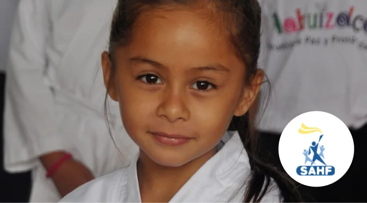 Young girl smiling while wearing a white martial arts uniform; SAHF logo in the corner.