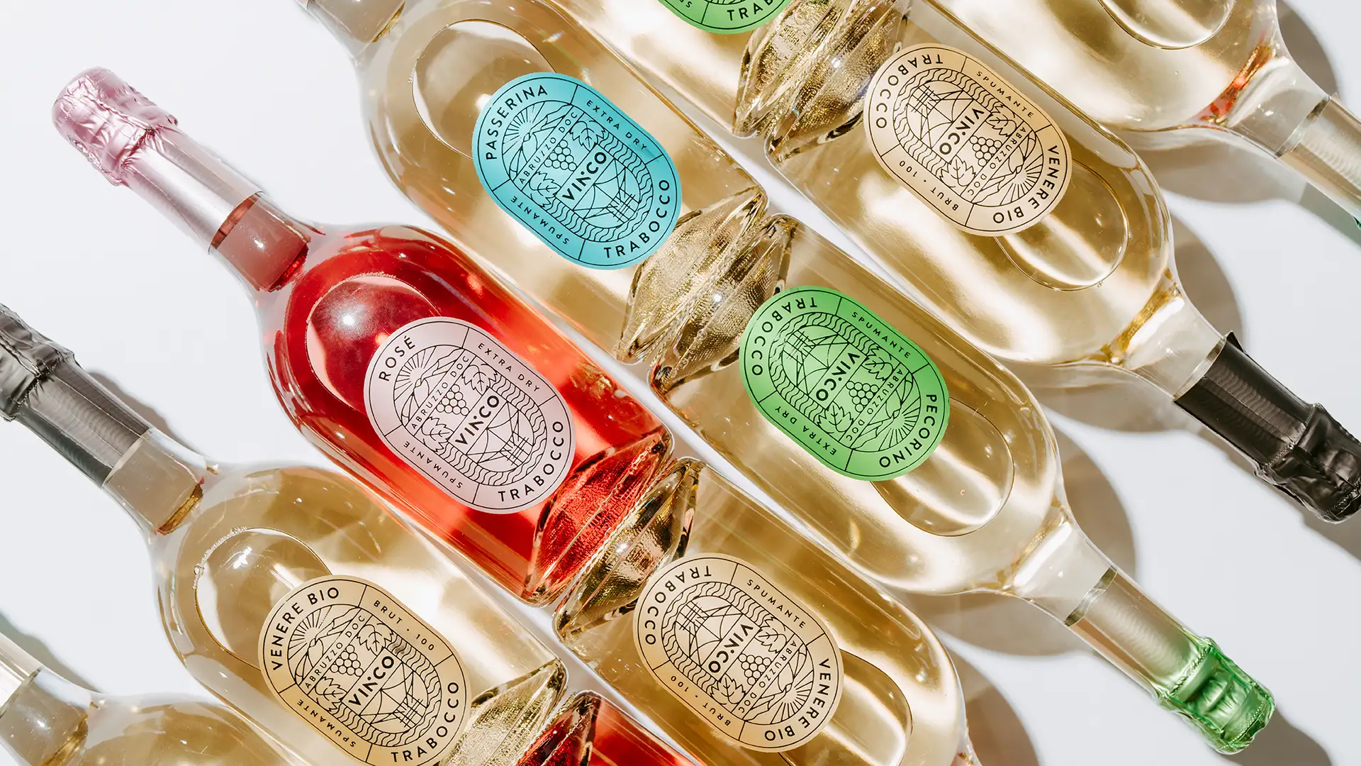 Vista ravvicinata delle bottiglie della gamma Vinco Trabocco in fila, con le etichette colorate (Passerina, Rosé, Pecorino, Venere Bio) in evidenza