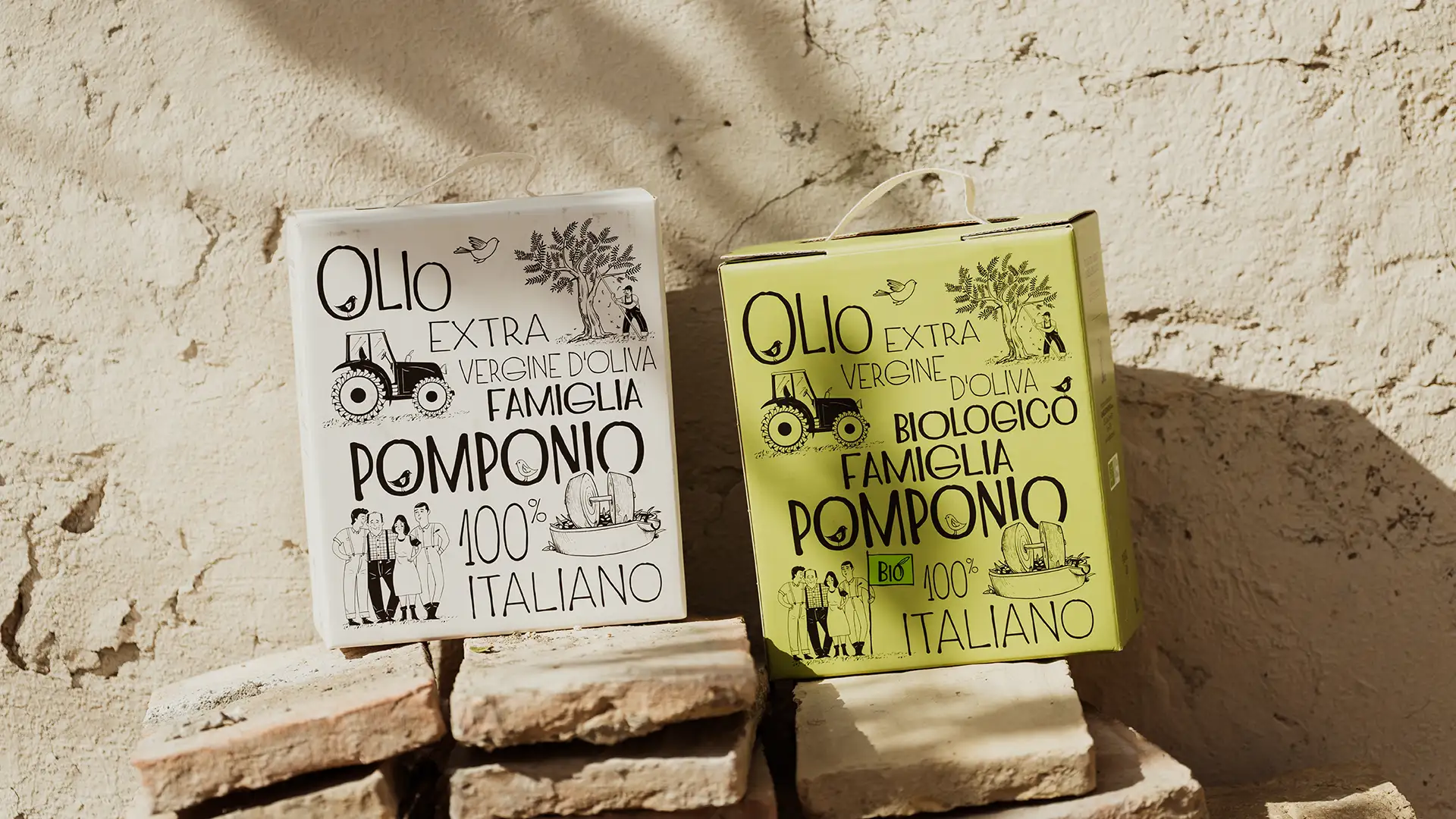 Due bag-in-box di Olio Extravergine Famiglia Pomponio (classico e biologico) appoggiati su una pietra rustica davanti a un muro antico