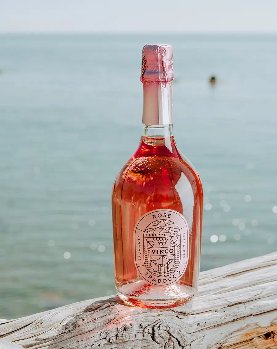 Bottiglia di Vinco Spumante Rosé appoggiata su un trabocco con il mare dell'Abruzzo sullo sfondo