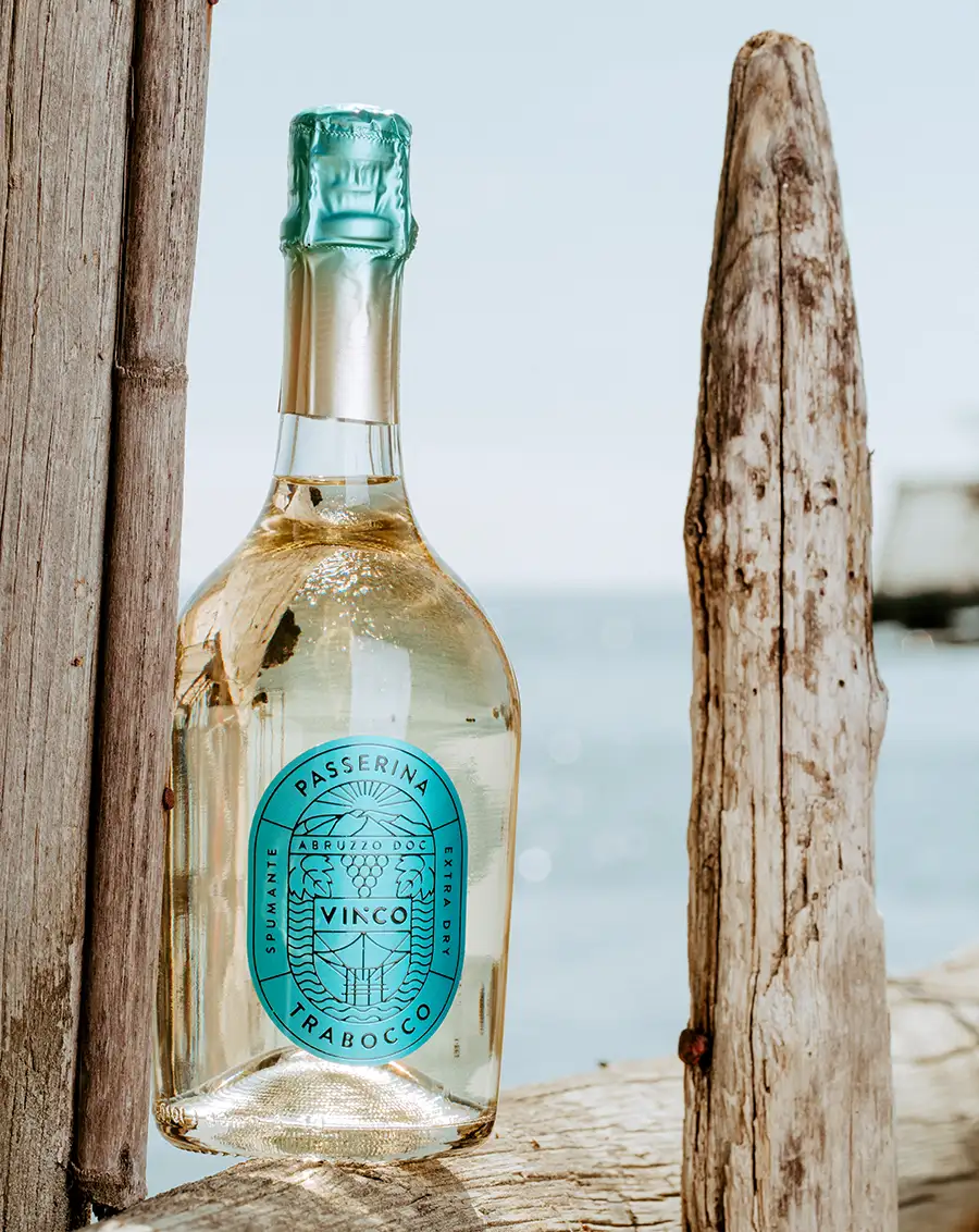 Bottiglia di Vinco Spumante Passerina Trabocco in verticale tra i pali in legno di un trabocco abruzzese