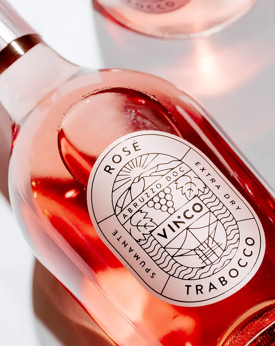 Primo piano di una bottiglia di vino Vinco Spumante Rosé in posizione orizzontale, con un'elegante etichetta decorata con motivi di uva e foglie.