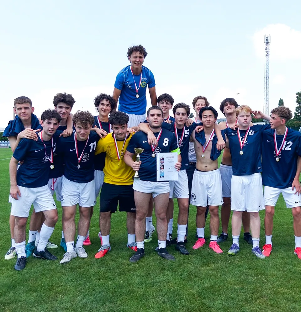 Gruppenfoto von jungen Männern in Fußballdressen mit Medaillen um den Hals, ein Spieler hält einen Pokal und eine Urkunde.