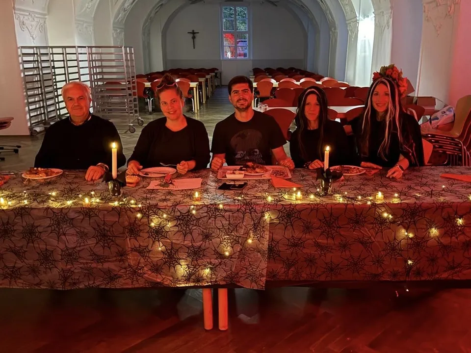 Five people sitting at a decorated, candlelit table with spider web patterns and string lights, in an arched, dimly lit room.