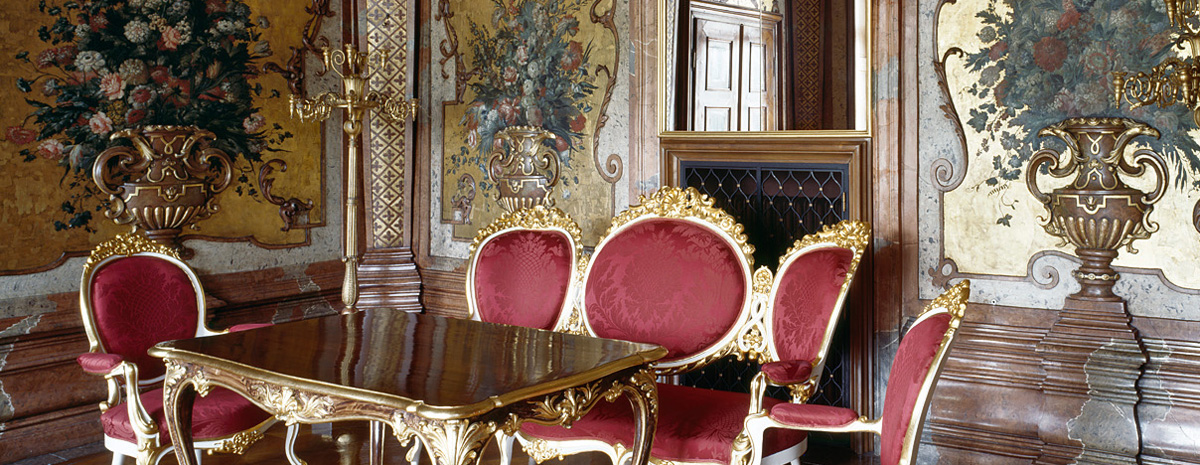 Aufnahme eines historischen barocken Raumes mit roten Stühlen, einem Marmortisch und goldenem Wanddekor