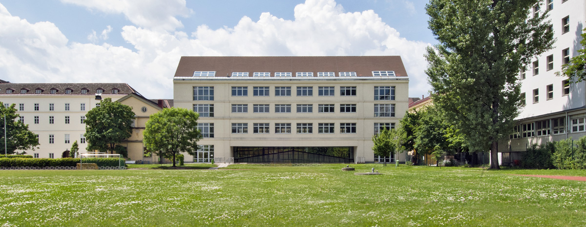 Modernes Gebäude unmittelbar angrenzend an historisches Gebäude mit satter grüner Wiese und Bäumen im Vordergrund.