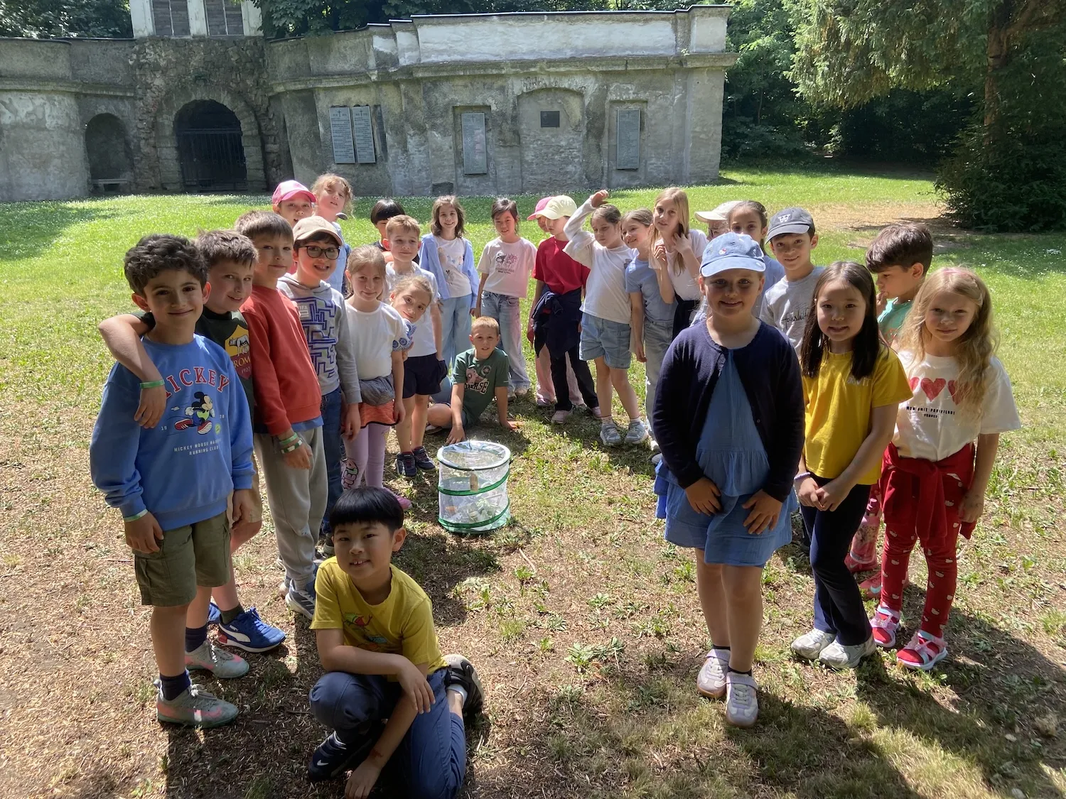 Gruppe von Kindern an einem sonnigen Tag um einen Netzkorb stehend mit historischem Denkmal im Hintergrund