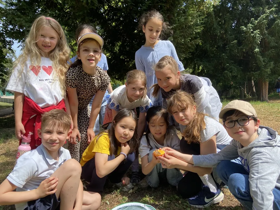 Gruppe von Kindern, die um eine halbe Orange herum stehen und hocken, auf der ein Schmetterling sitzt.