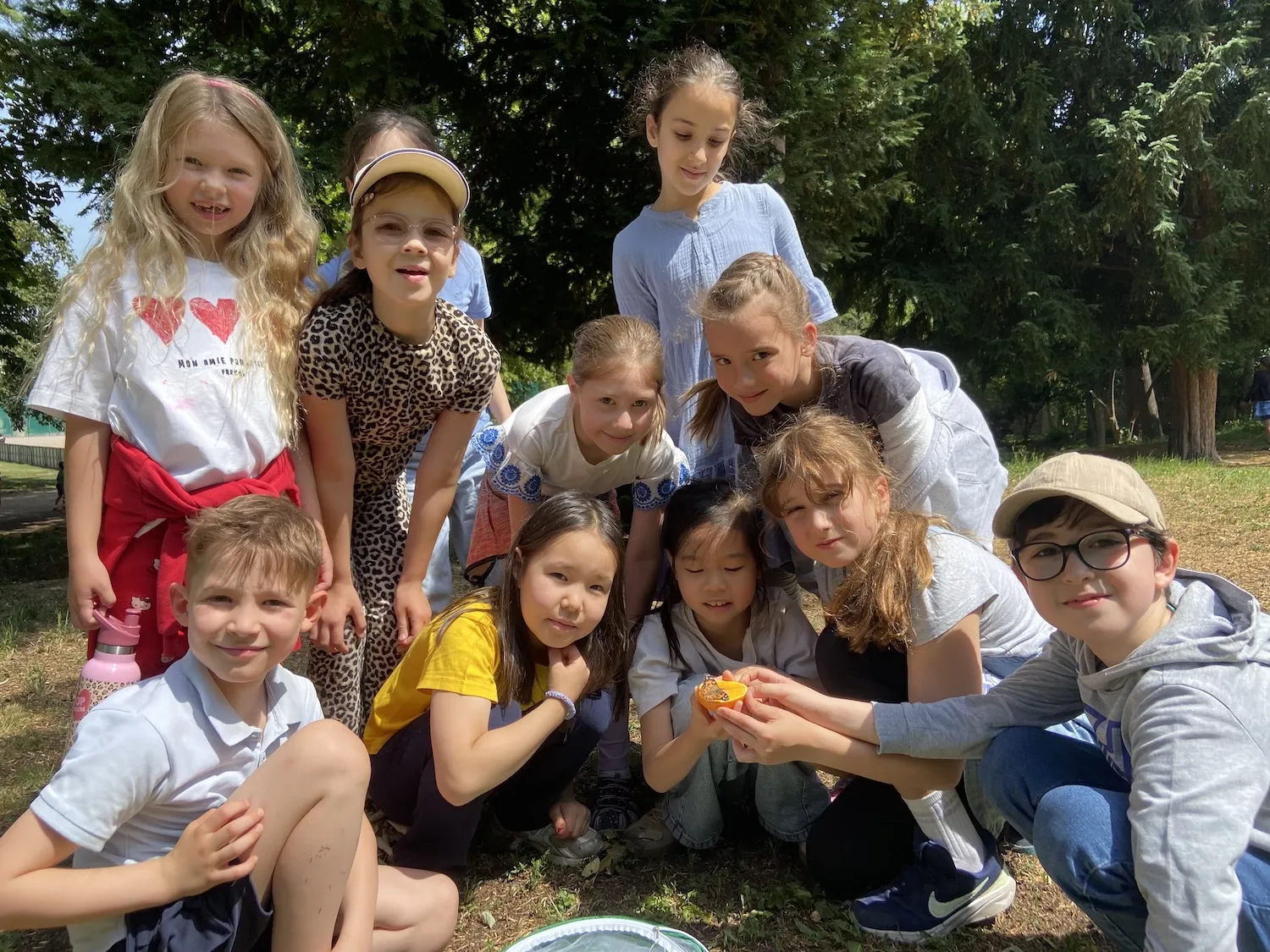 Gruppe von Kindern, die um eine halbe Orange herum stehen und hocken, auf der ein Schmetterling sitzt.