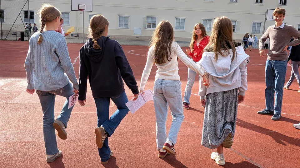 Vier Mädchen von hinten auf einem Sportplatz auf einem Bein stehend.