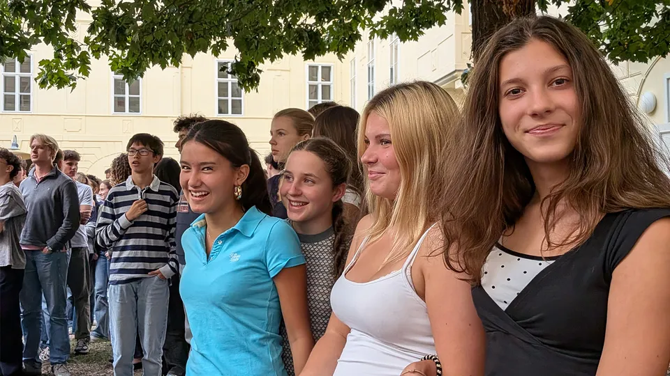 Gruppe von Jugendlichen in einem begrünten Innenhof stehend. Zwei Mädchen blicken lachend in die Kamera.