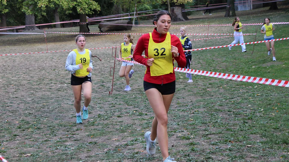Junge Mädchen mit Startnummer auf einer Laufbahn und Querfeldein laufend.
