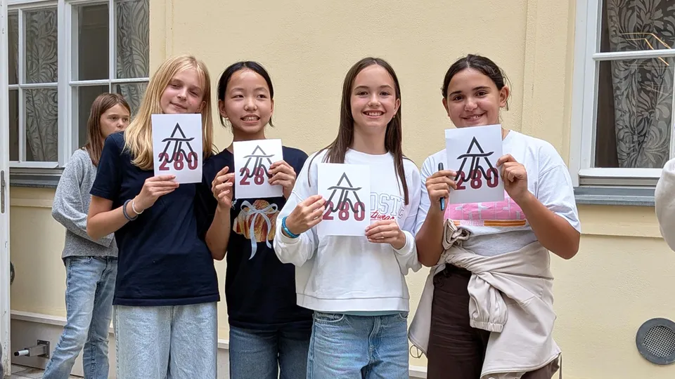 Gruppe von gut gelaunten Mädchen, die eine Karte mit der Zahl 280 und dem Theresianum Signet in die Höhe halten.