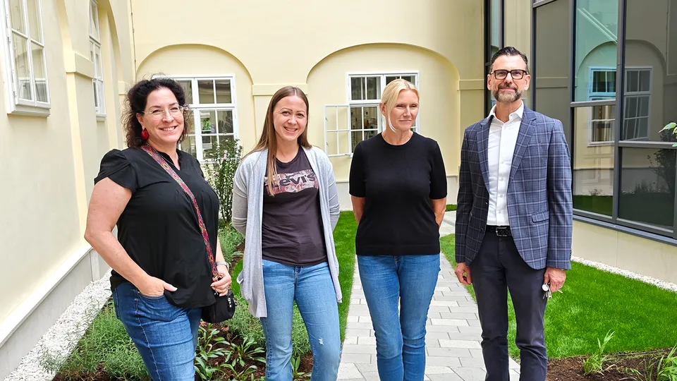 Ein Mann und drei Frauen in einem historischen renovierten Innenhof stehend und in die Kamera lachend.