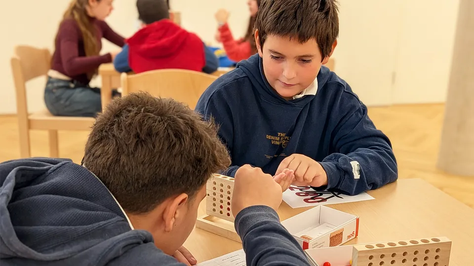 Zwei junge Burschen an einem Tisch sitzend, die konzentriert vier gewinnt spielen.