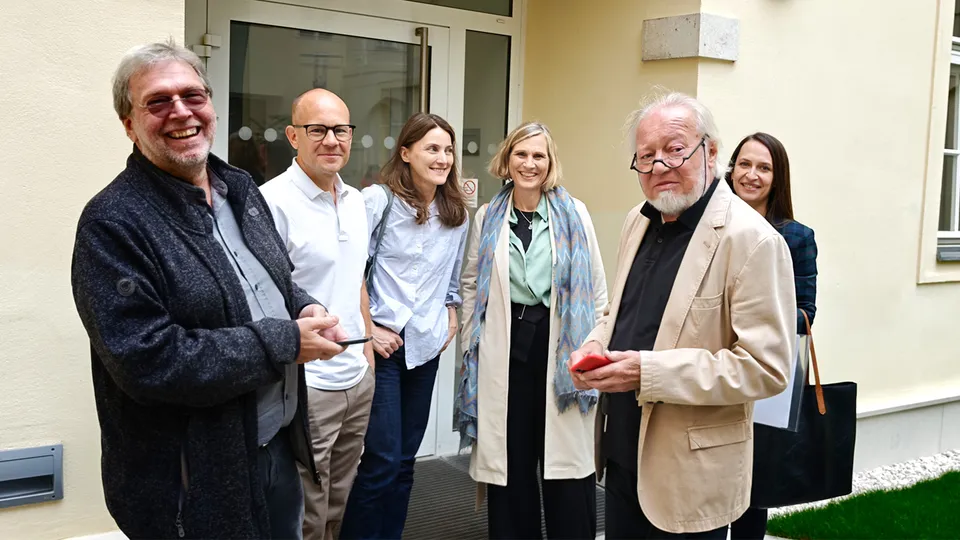 Gruppe von Frauen und Männern in einem Gebäudeinnenhof stehend und gut gelaunt in die Kamera lachend.