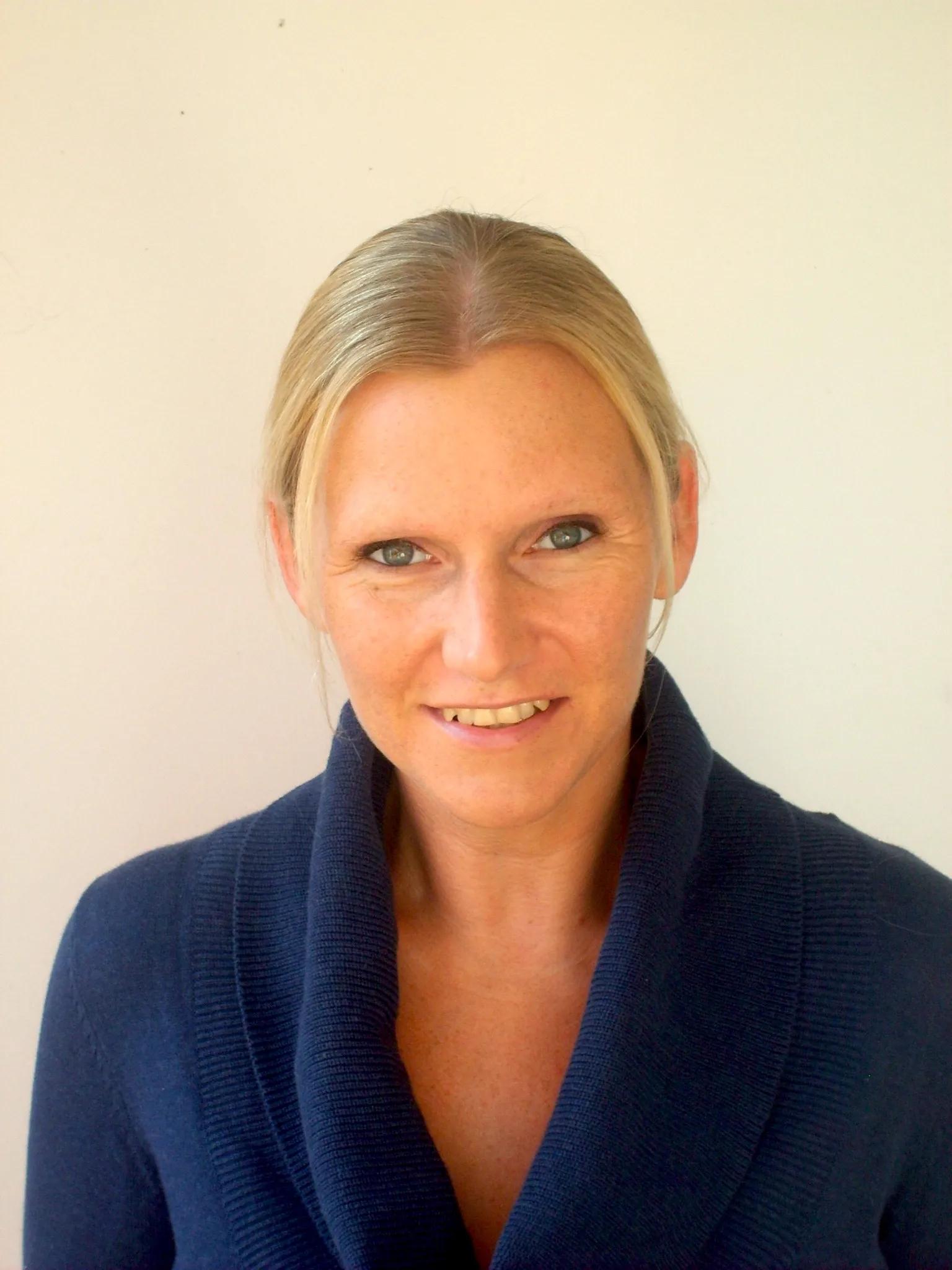 Portraitfoto einer blonden attraktiven Frau mit Haaren glatt nach hinten und dunkelblauer Strickjacke mit V-Ausschnitt