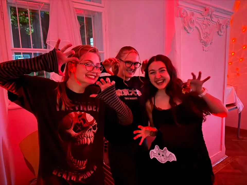 Three people in Halloween-themed clothing, smiling and making monster poses in a room with red lighting.