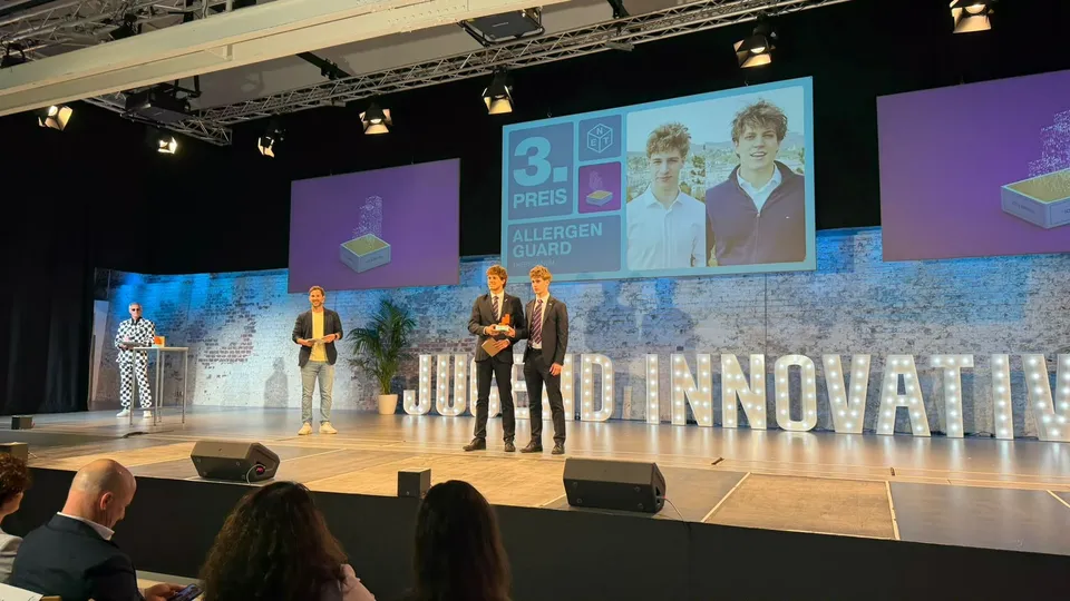 Vier Personen auf einer Bühne mit Bildschim im Hintergrund und dem Schriftzug Jugend Innovativ