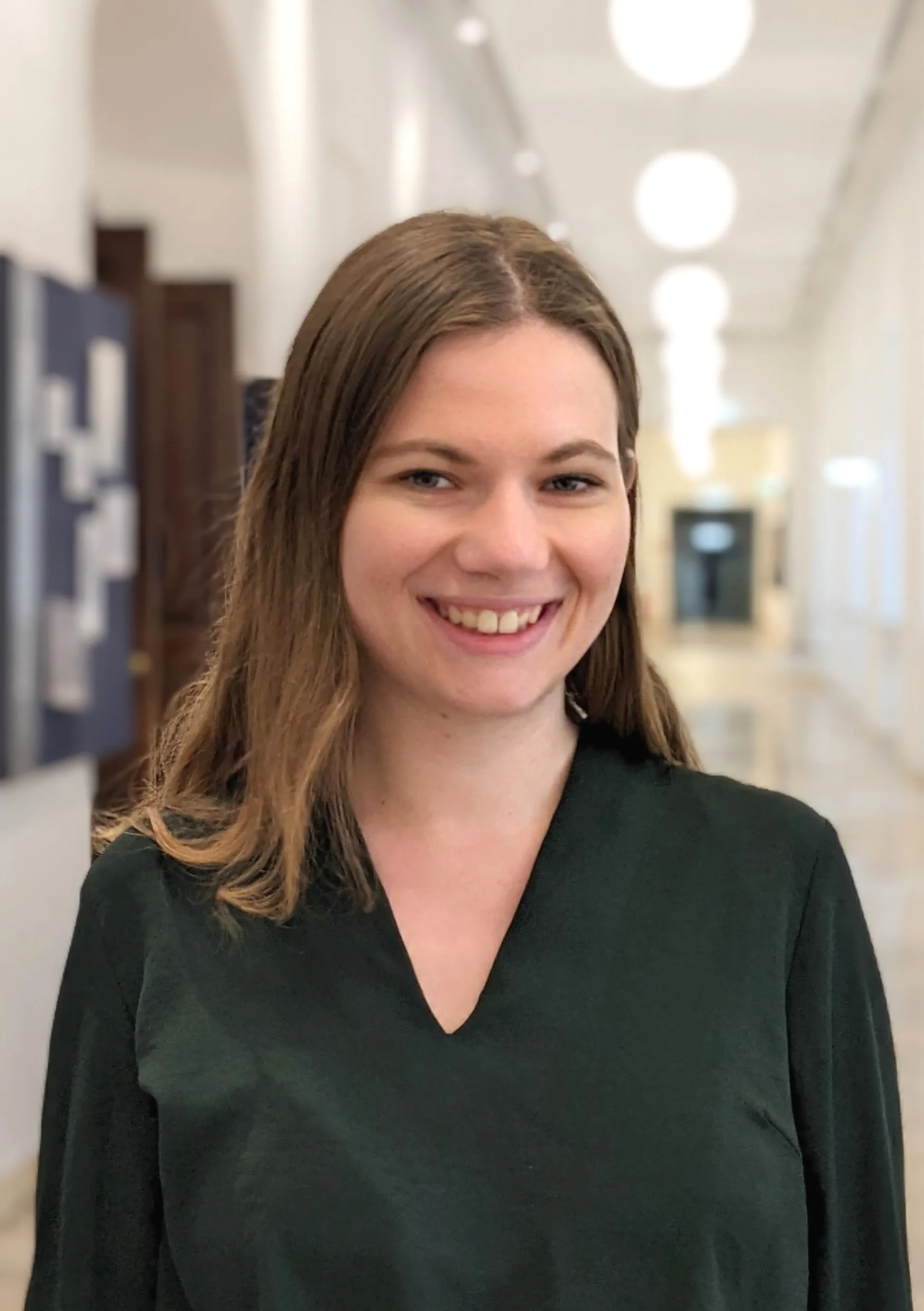 Junge lächelnde Frau mit langen, glatten braunen Haaren, die ein dunkles Oberteil trägt.