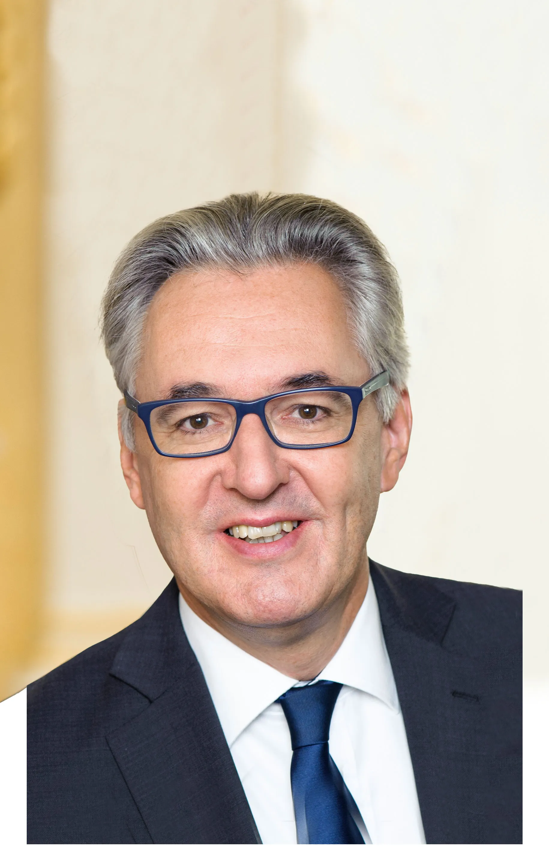 eleganter reifer Mann mit grauem Harr, blauer Brille und dunklem Anzug mit blauer Krawatte