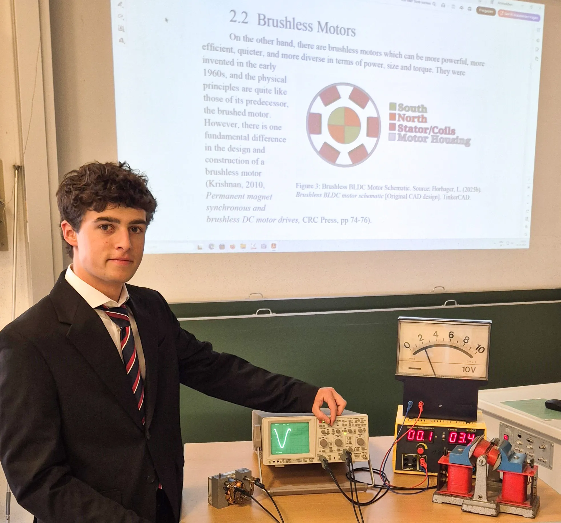 Junger Mann in Anzug und mit Krawatte präsentiert ein technisches Gerät, im Hintergrund mit Informationen in englisch zu Brushless Motors