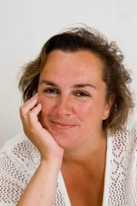 Porträt einer Frau mit mittellangen brünetten Haaren, das Gesicht in einer Hand abgestützt, selbstbewusst und vertrauenserweckend in die Kamera blickend