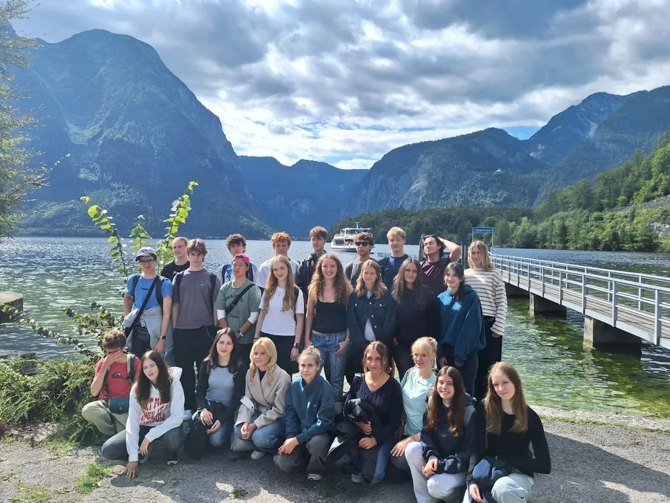 A group of young people poses in front of a scenic lake with mountains in the background and a dock extending into the water.
