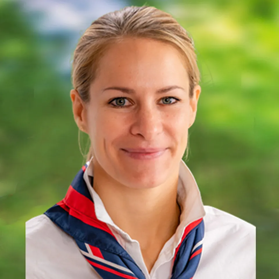 Frau mit einem leichten Lächeln, die eine weiße Bluse und ein blau‑rotes Tuch trägt.